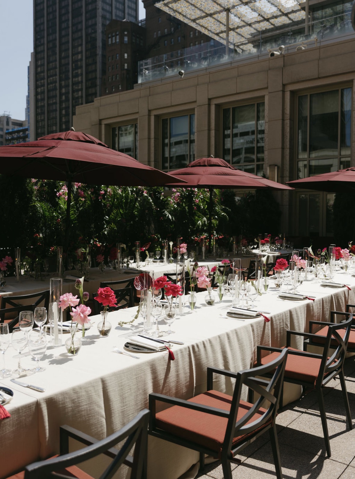 A long table set for a gathering under red umbrellas